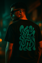 Person wearing a black t-shirt with a glowing green design on the back, standing against a dark background.