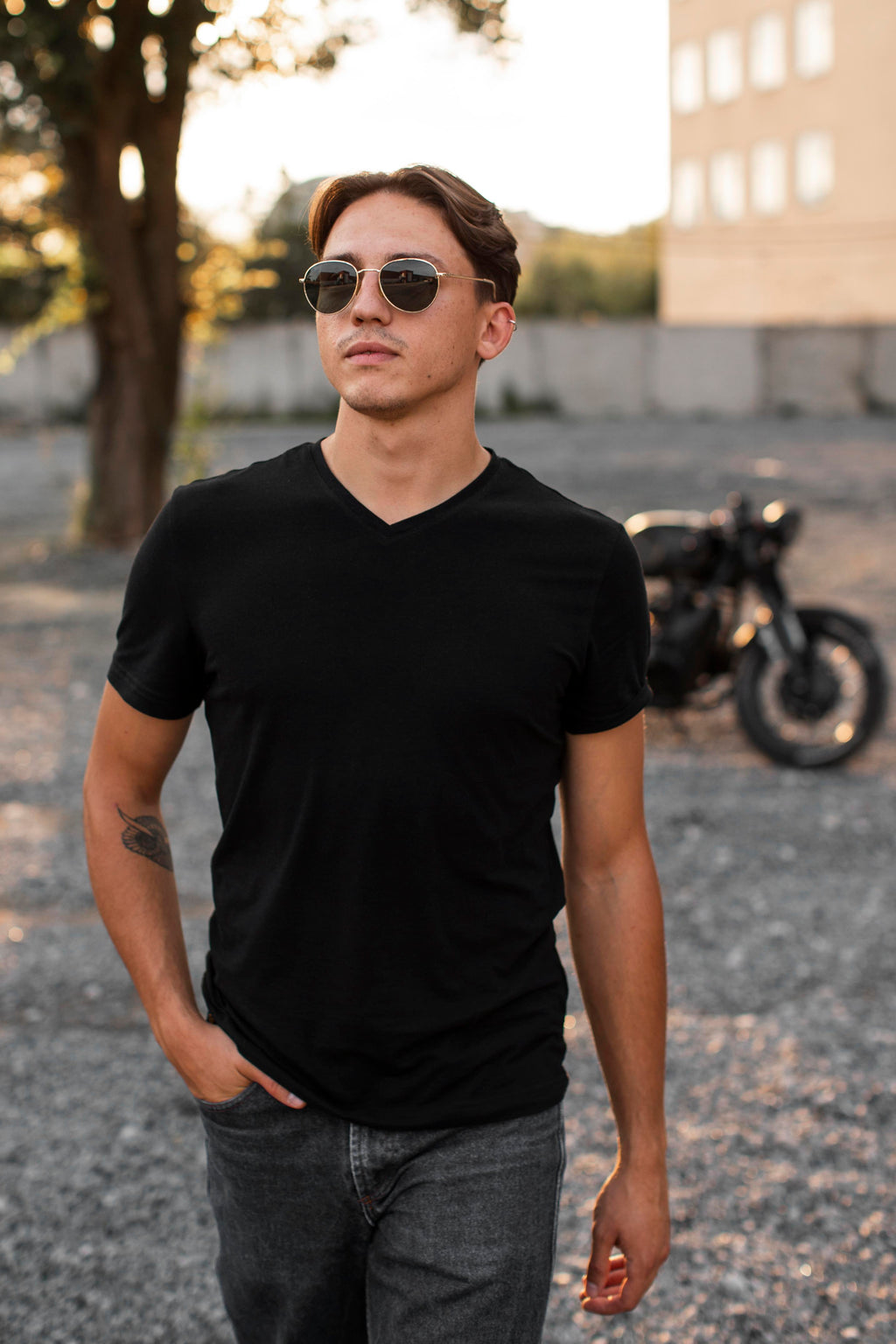 Man wearing a black t-shirt and sunglasses standing in front of a motorcycle.