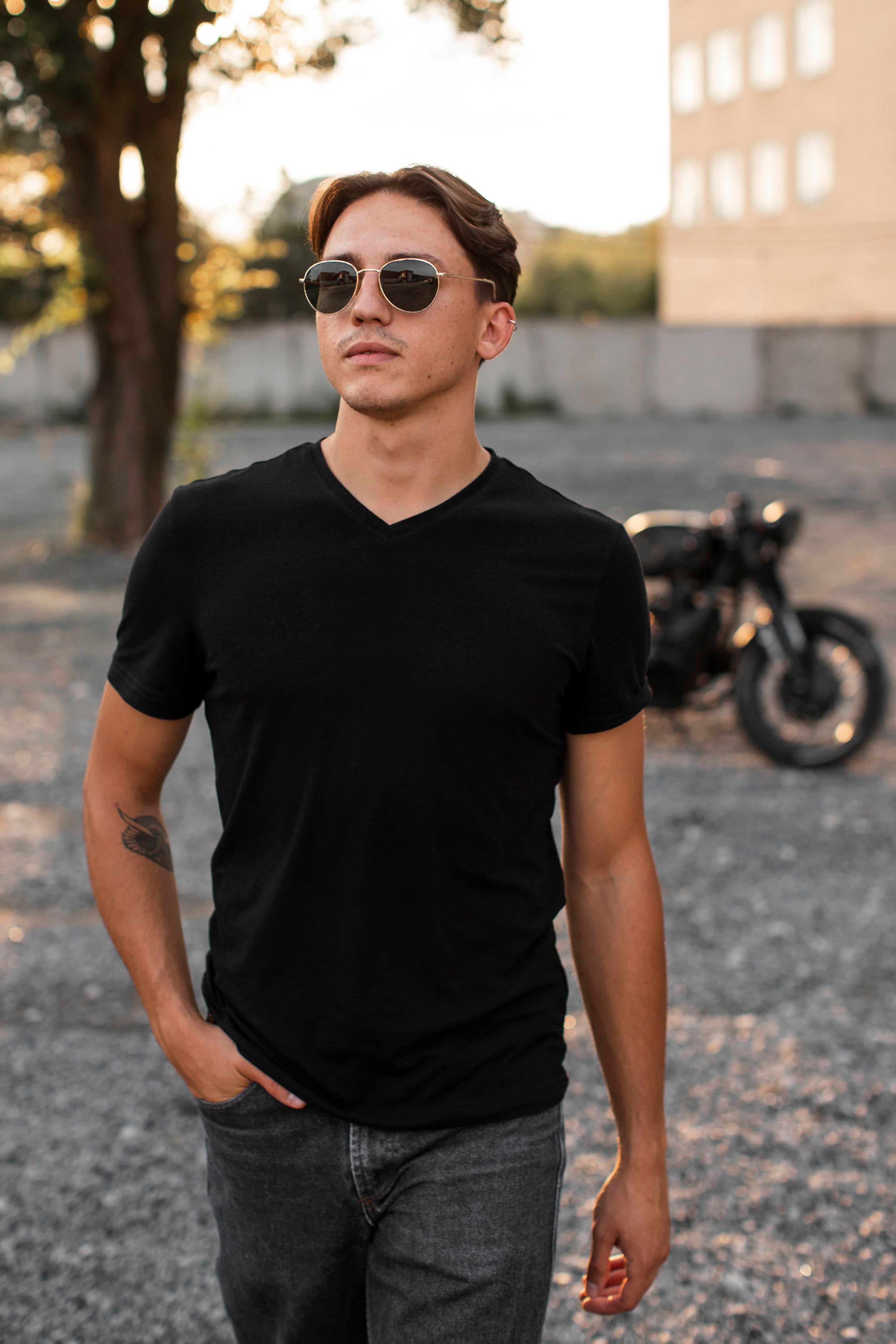 Man wearing a black t-shirt and sunglasses standing in front of a motorcycle.
